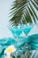 Exotic tropical Blue Curacao cocktail drink in a glasses with Plumeria frangipani flower, palm leaf on the background