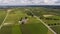 Expansive Aerial View Of Rolling Green Agricultural Fields, Farm Buildings, And A Long Country Road