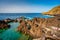 Expansive body of water situated near a large rock formation, with jutting cliffs and rugged terrain