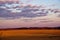 An expansive view of ploughed farmland at sunset, trees in backdrop