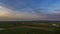 Expansive View Of Rural Landscape At Twilight With Patchwork Fields, Sparse Buildings, Colored Sky.