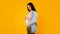 Expecting a baby. Portrait of happy pregnant lady tenderly touching belly and smiling, posing on yellow background