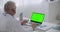 Experienced doctor is listening patient or colleague by video call on laptop with green display for chroma key