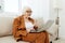 an experienced, elderly woman is sitting on a sofa in a brown suit, holding a video conference on a laptop, passing on