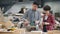 Experienced joiner teaching female apprentice to use belt sander polishing wood