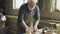 Experienced male potter is mixing and kneading clay on worktable while working in small workshop with professional