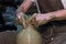 Experienced potter makes a large vase on a potter`s wheel. twisting a narrow neck. clay product