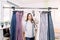 Experienced smiling female dressmaker standing near clothing rack with fashionable stylish handmade pants and thinking