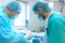 An experienced surgeon in a mask and gown operates in a sterile operating room with an assistant and an anesthesiologist..A group