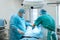 An experienced surgeon in a mask and gown operates in a sterile operating room with an assistant and an anesthesiologist..A group