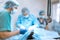 An experienced veterinarian in a mask and gown operates a pet dog in a sterile operating room with an assistant and an