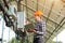 Expert is inspecting quality of solar panels. Man in hardhat standing with laptop near electrical equipment