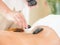 An expert masseuse at a spa salon puts hot stone on the back of an Asian woman to relieve tension from work