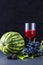 Exposition of fresh natural fruits, healthy food with many vitamin, watermelon, apple, grapes, glass of juice on black background.
