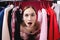 Expressive Caucasian young woman is very surprised looking out of clothes on hangers. Season of low sales prices and