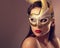 Expressive female model posing in carnival mask with red lipstick and looking vamp on empty copy space background. Closeup