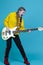 Expressive Positive Caucasian Teenager Guitar Musician Playing On Yellow Bass Guitar Posing In Fashionable Yellow Hoody Jacket