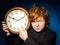Expressive red-haired teenage boy showing time on big clock