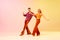 Expressive, talented, emotional couple, man and woman in stylish clothes dancing disco dance against gradient pink