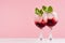 Exquisite arctic red alcoholic liquors with ice cubes, blueberry, green mint in two wineglasses on white wood table and pink.