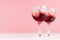 Exquisite arctic red alcoholic liquors with ice cubes, blueberry in two wineglasses on white wood table and pastel pink wall.