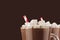 Exquisite chocolate dessert with marshmallows and red striped straw closeup, details, top section on dark brown background.