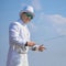 Exquisite fishing. Fisherman in white suit catch fish by spinning rod at lake