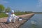 Exquisite fishing. Fisherman in white suite catch fish by spinning rod at lake