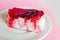 Exquisite souffle cake with lingonberry jelly, with berry glaze and coconut on a white plate, close-up, pink background