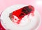 Exquisite souffle cake with lingonberry jelly, with berry glaze and coconut on a white plate, close-up, pink background