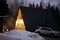 Exterior at dusk of modern triangle log cabin in the mountains with bonfire and parked suv car