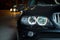 Exterior of a modern car . Black dark luxury car in the night road with angry bright headlight front for wallpaper and background