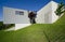 Exterior of a modern colored concrete house. A cube in the middle of the green. Profile view