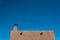 Exterior red adobe framed by blue sky, chimney and exposed beams