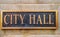 Exterior sign that reads `City Hall ` in brass lettering