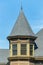 Exterior turret or spire with beige stucco home or house and gray slatted roof with spike on pinacle