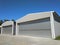 Exterior of two metal hangar for storage under blue sky. Side view of two garages with closed rolling doors with concrete blocked