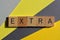 Extra, word in wooden alphabet letters isolated on grey and yellow background