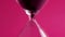 Extreme close-up of black sand running down through hourglass on a crimson background. A concept the sand runs out to