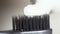 Extreme close up for a black toothbrush with white toothpaste being squeezed on it on beige background. Media. The black