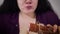 Extreme close-up of fat Caucasian woman greedily eating sausage. Obese brunette girl hungrily biting unhealthy food