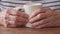 Extreme Close up on older Caucasian womans hands on coffee cup at wood table