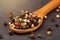 Extreme close up a of peppercorn mix in a wooden spoon on a dark stone kitchen board