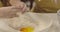 Extreme close-up of plate with white flour. Adult female Caucasian hands breaking egg, little girl smashing another egg