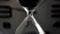 Extreme close up of a transparent hourglass with flowing black sand on blur dial background. Old classic timer. Time