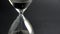 Extreme close up of a transparent hourglass with flowing black sand on blur dial background. Old classic timer. Time