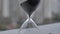 Extreme close up of a transparent hourglass with flowing black sand on blur dial background. Old classic timer. Time