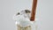 Extreme close-up whipped cream with cinnamon stick spinning at white background. Closeup glass of oat cereals with