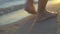 Extreme close-up of young female Caucasian feet walking along sandy beach at sunset. Unrecognizable slim barefoot woman