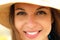 Extreme close up of young model face with straw hat smiling at camera under summer rays sun on the beach.